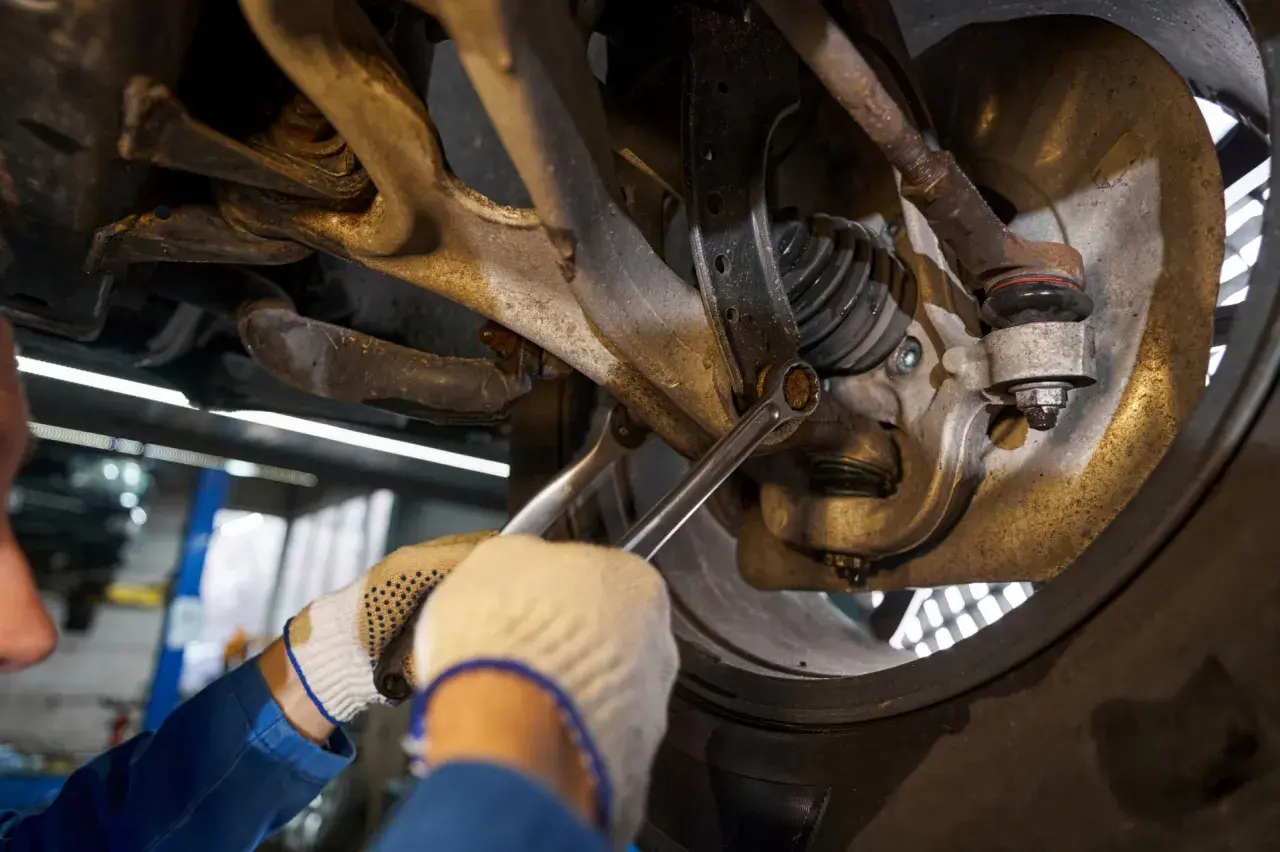 Mechanik w rękawiczkach dokręca śrubę w zawieszeniu samochodu.