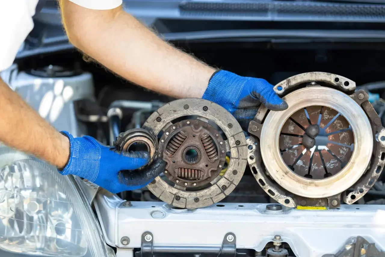 Wymiana sprzęgła krok po kroku: mechanik w niebieskich rękawiczkach trzyma zużyte części.