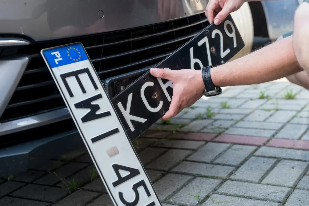 Wymiana tablic rejestracyjnych. Jedna tablica z oznaczeniem PL jest już zamontowana, druga jest wkładana.