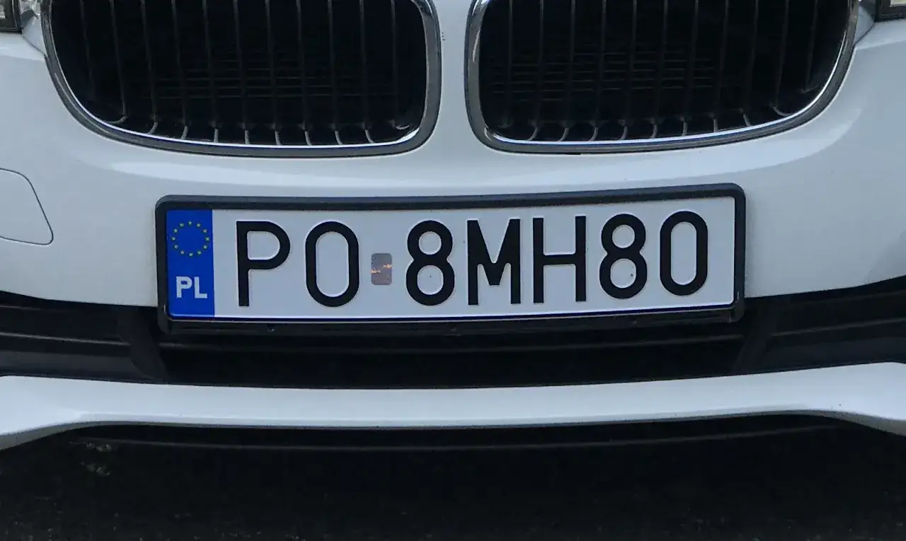 Polskie tablice rejestracyjne z numerem PO 8MH80 na białym samochodzie.