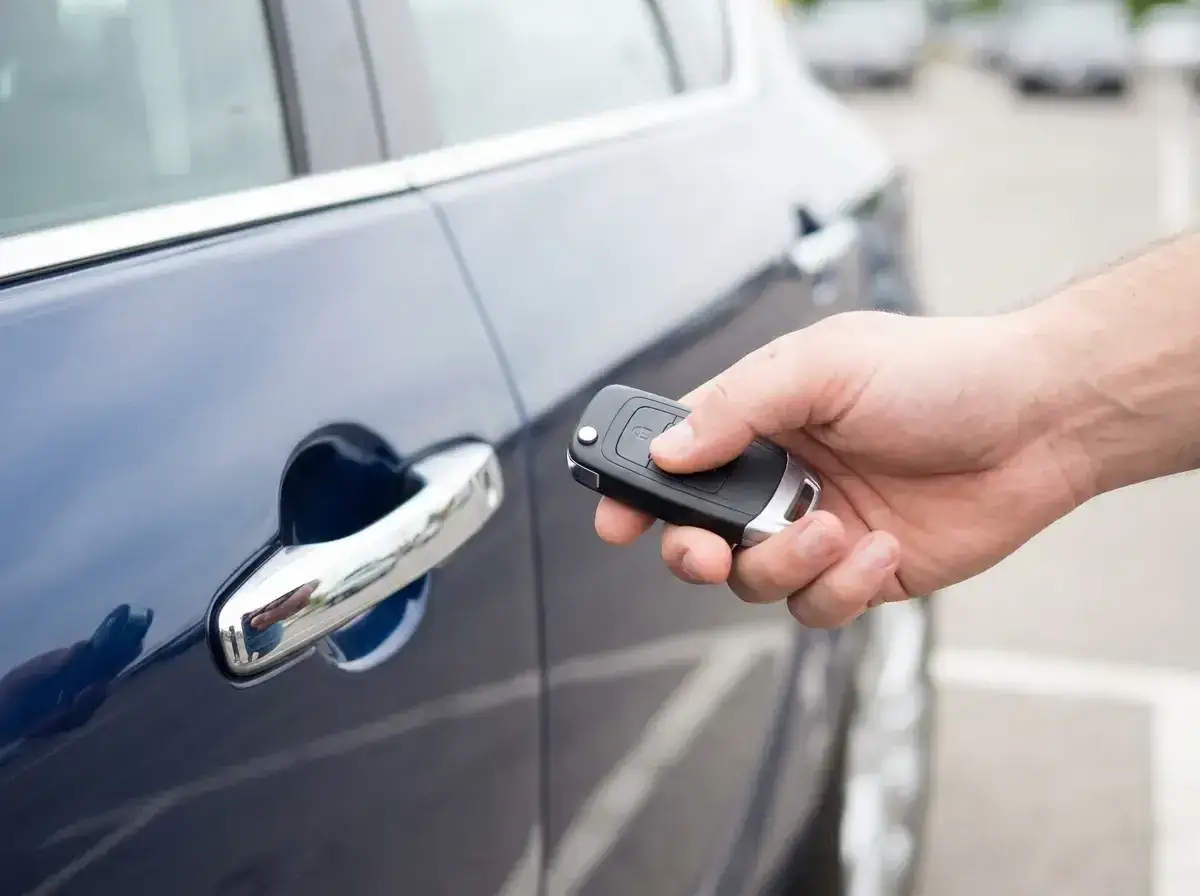 Dłoń z kluczykiem zbliża się do drzwi samochodu, aktywując system keyless.