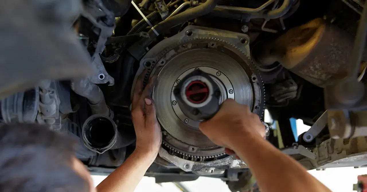Mechanik wykonuje wymianę sprzęgła krok po kroku, demontując koło zamachowe.