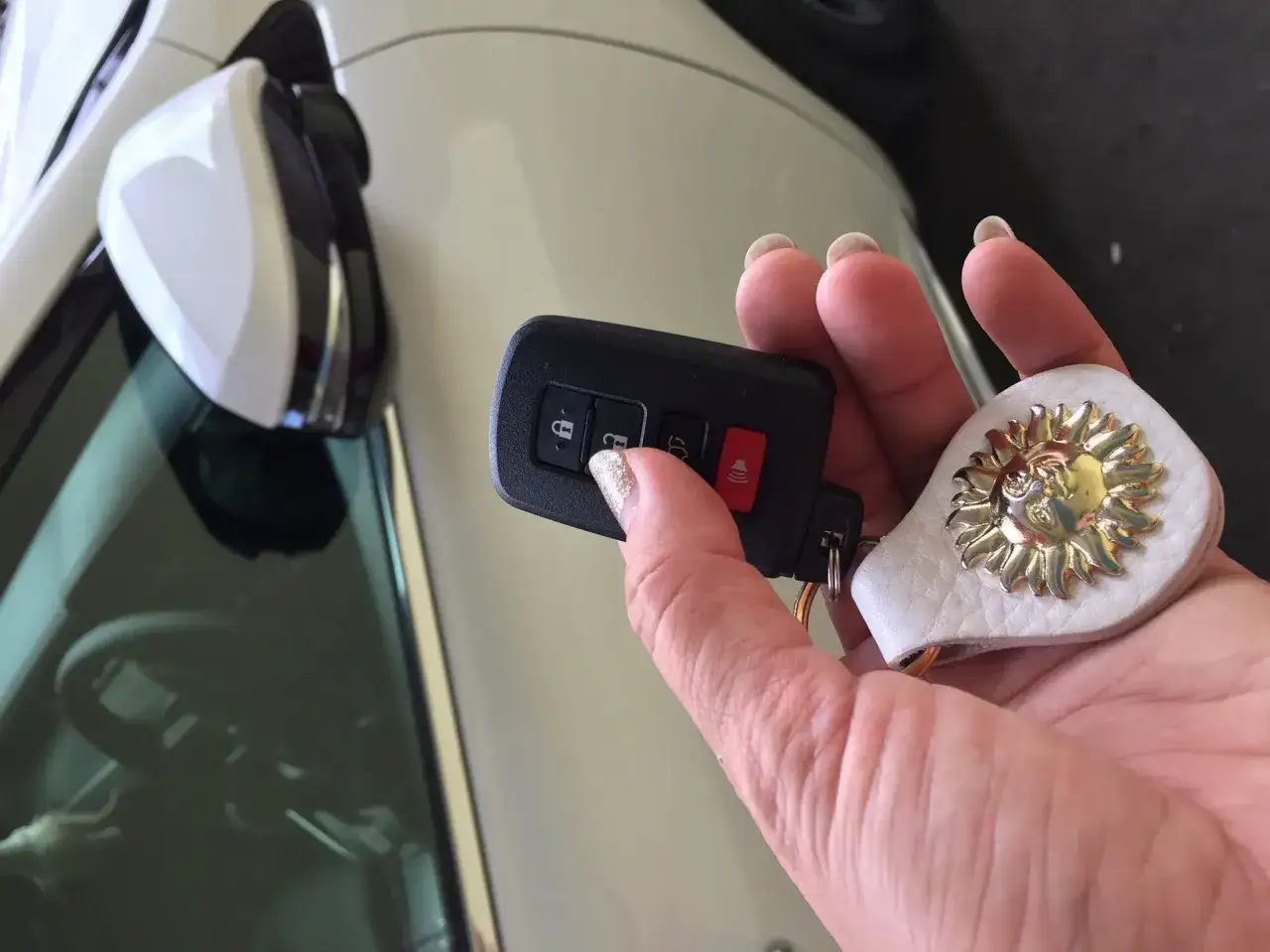 Dłoń z breloczkiem w kształcie słońca próbuje otworzyć auto, ale auto nie reaguje na kluczyk.
