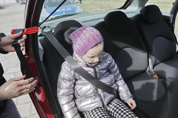 Dziecko w samochodzie, zapinany pas bezpieczeństwa. W tle radiowóz policji. To inteligentne rozwiązanie dla bezpieczeństwa najmłodszych.