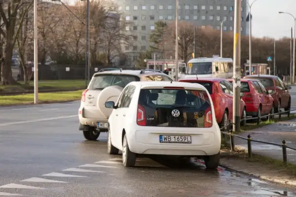 Biały Volkswagen Up i inne samochody stoją na pasach, blokując skrzyżowanie.