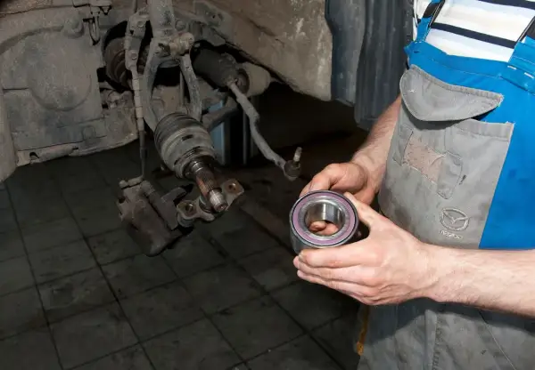 Mechanik trzyma nowe łożysko koła, przygotowując się do wymiany. Pokazuje, jak sprawdzić łożysko w kole.