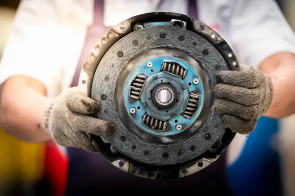 Mechanik trzyma w rękawicach odwrotnie założoną tarczę sprzęgła, gotową do montażu.