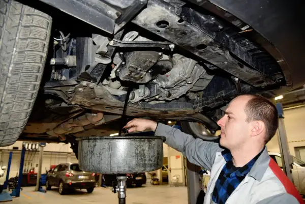 Mechanik spuszcza olej z silnika. Pamiętaj, co ile wymiana oleju jest kluczowa dla żywotności auta.