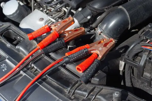 Kable rozruchowe podłączone do akumulatora, bo auto nie odpala. Miedziane klamry i czerwono-czarne uchwyty.